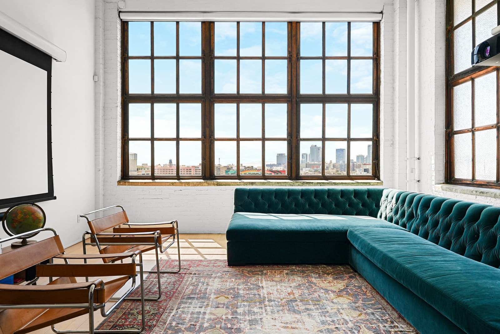 Steel loft windows with the skyline beyond, velvet sofa and leather chairs