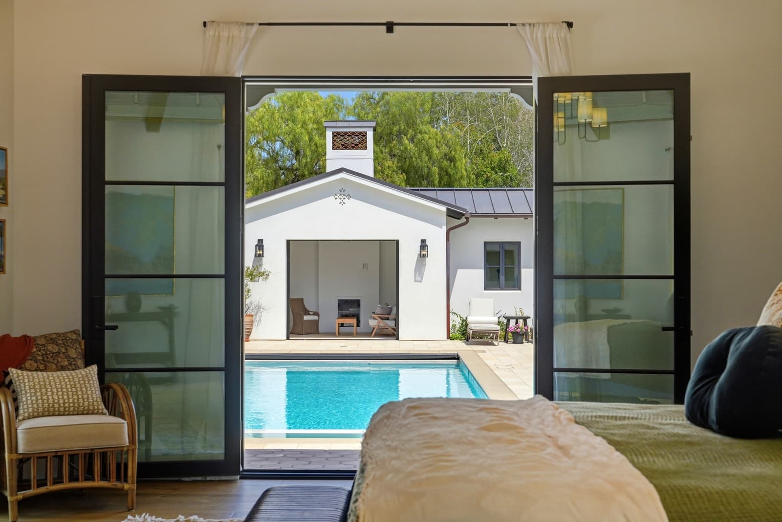 Bedroom opening through steel-framed doors to a pool house