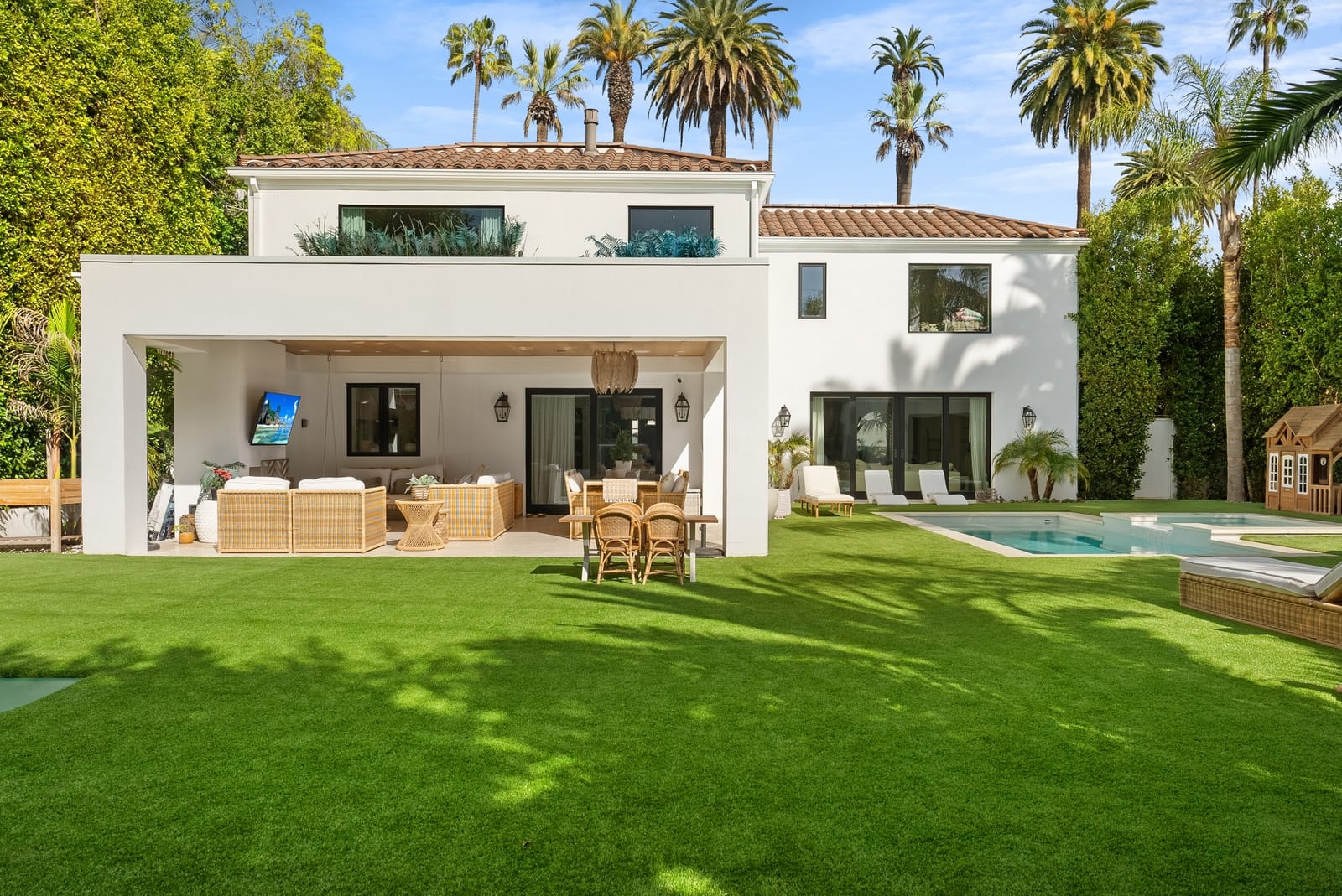 Rear of a white Spanish estate across the lawn, pool and covered patio