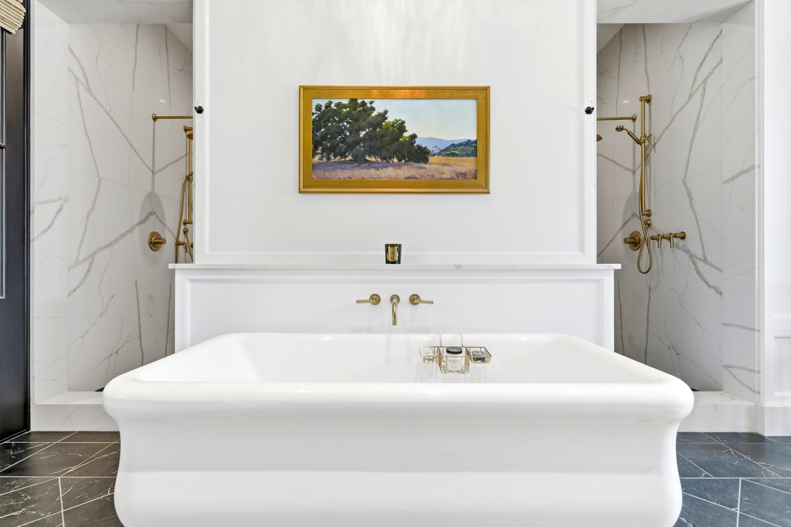 Freestanding tub with brass fixtures under a landscape painting, seen straight on