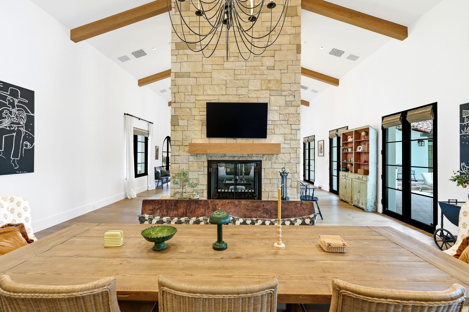 Great room under wood beams with a stone fireplace and chandeliers, seen straight on