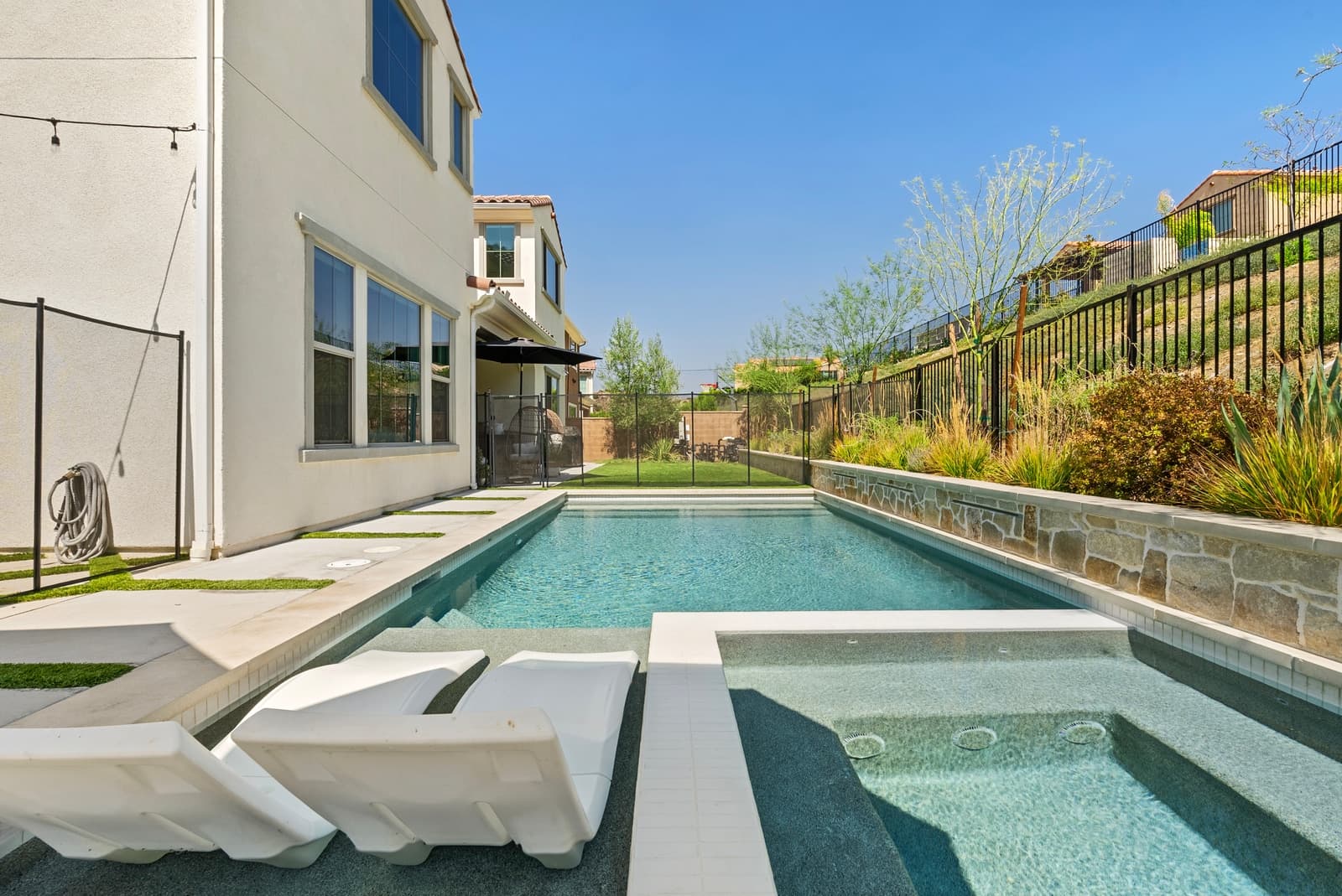 Modern pool with in-water loungers and a stone wall, Canoga Park