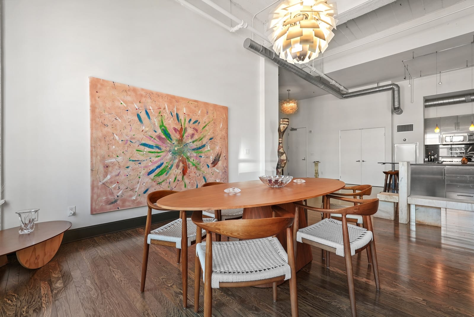 Loft dining room under a sculptural pendant and a large painting