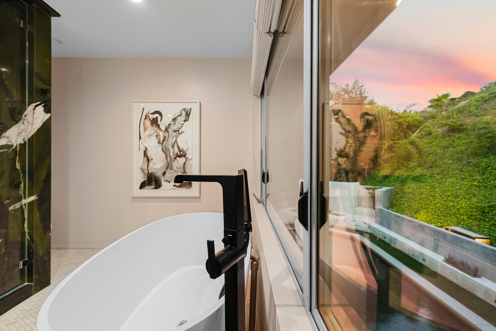Freestanding tub against floor-to-ceiling glass with hillside greenery
