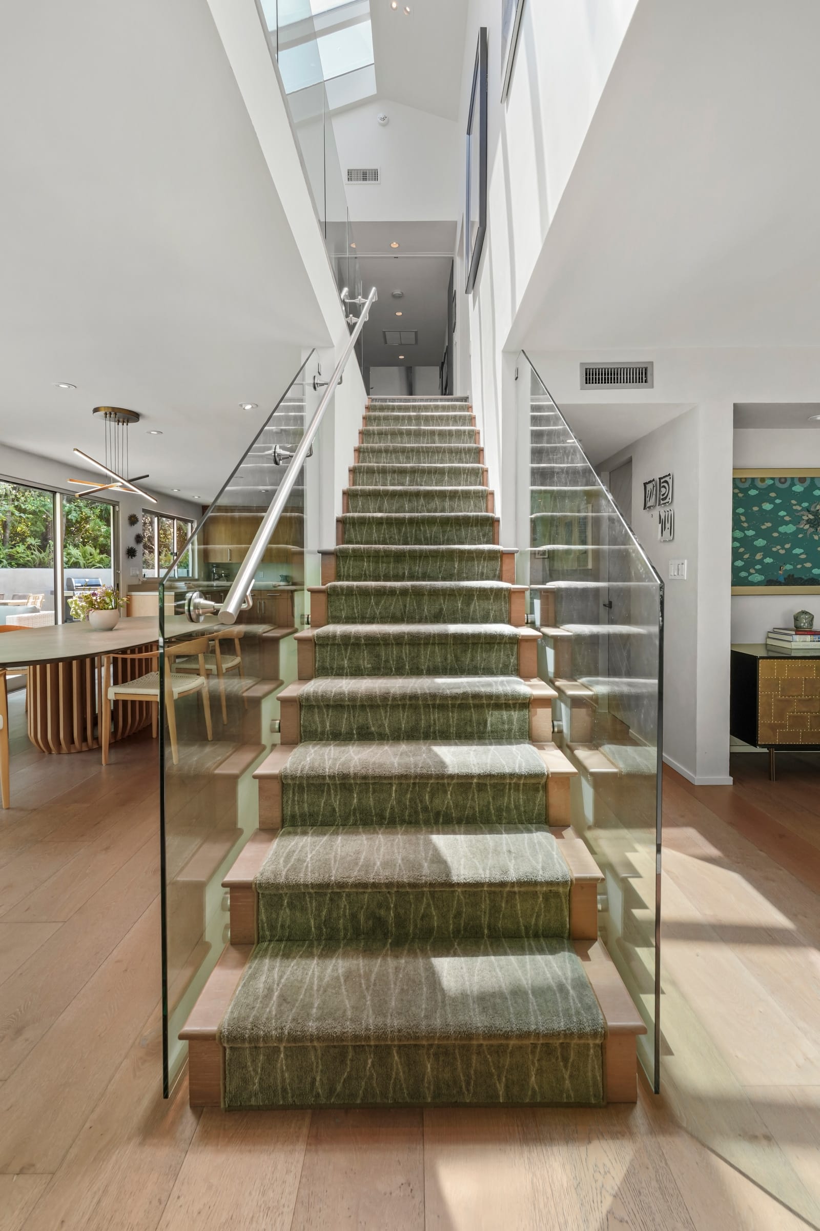 Glass-railed staircase with a patterned runner, dining room beyond
