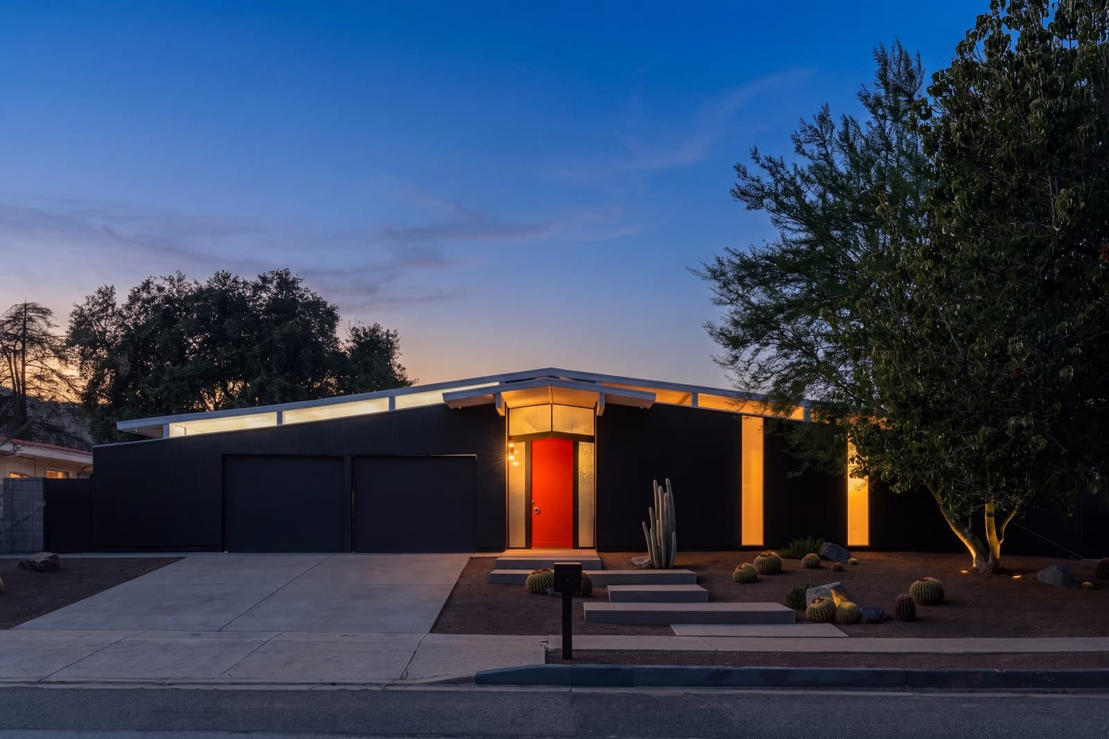 Eichler front at twilight, the red door and clerestory windows glowing in a dark facade
