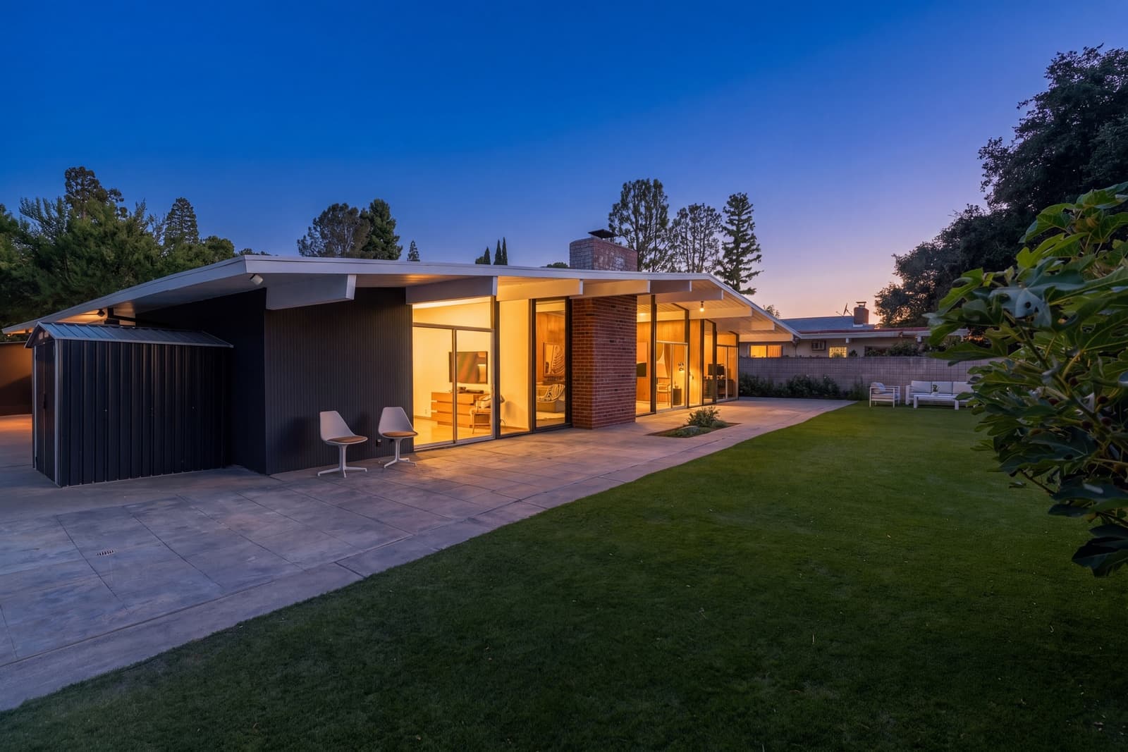 Rear of a midcentury home at twilight, every room lit through the glass