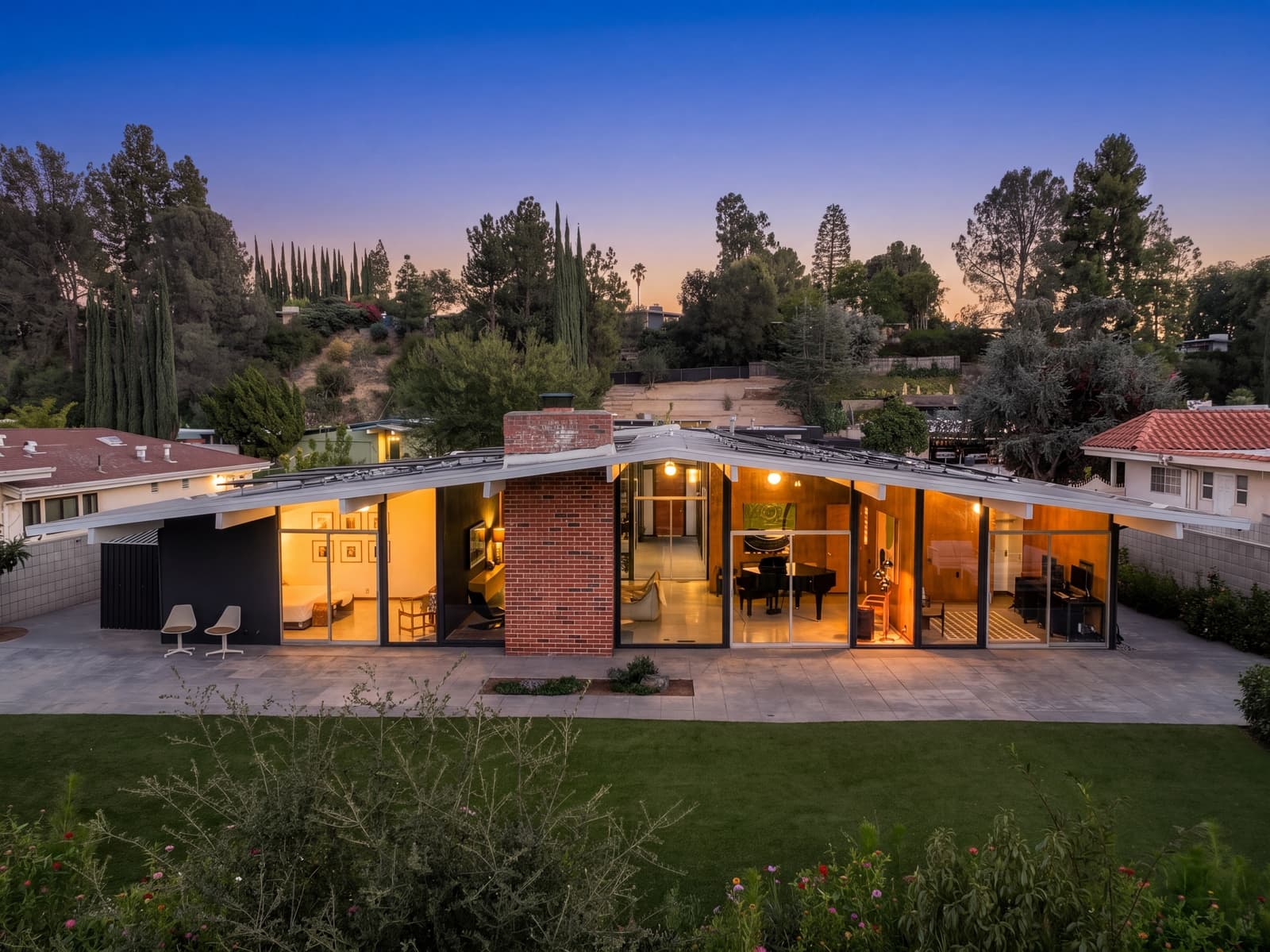 Rear glass wall glowing at twilight, cypress along the ridge behind