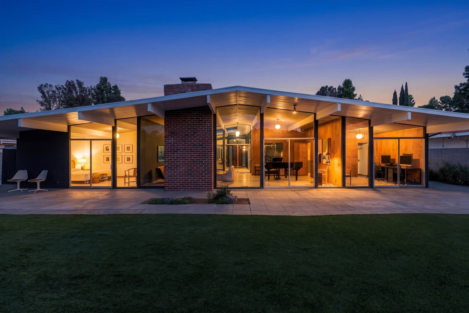 Glass rear wall lit from inside at twilight, brick chimney and lawn