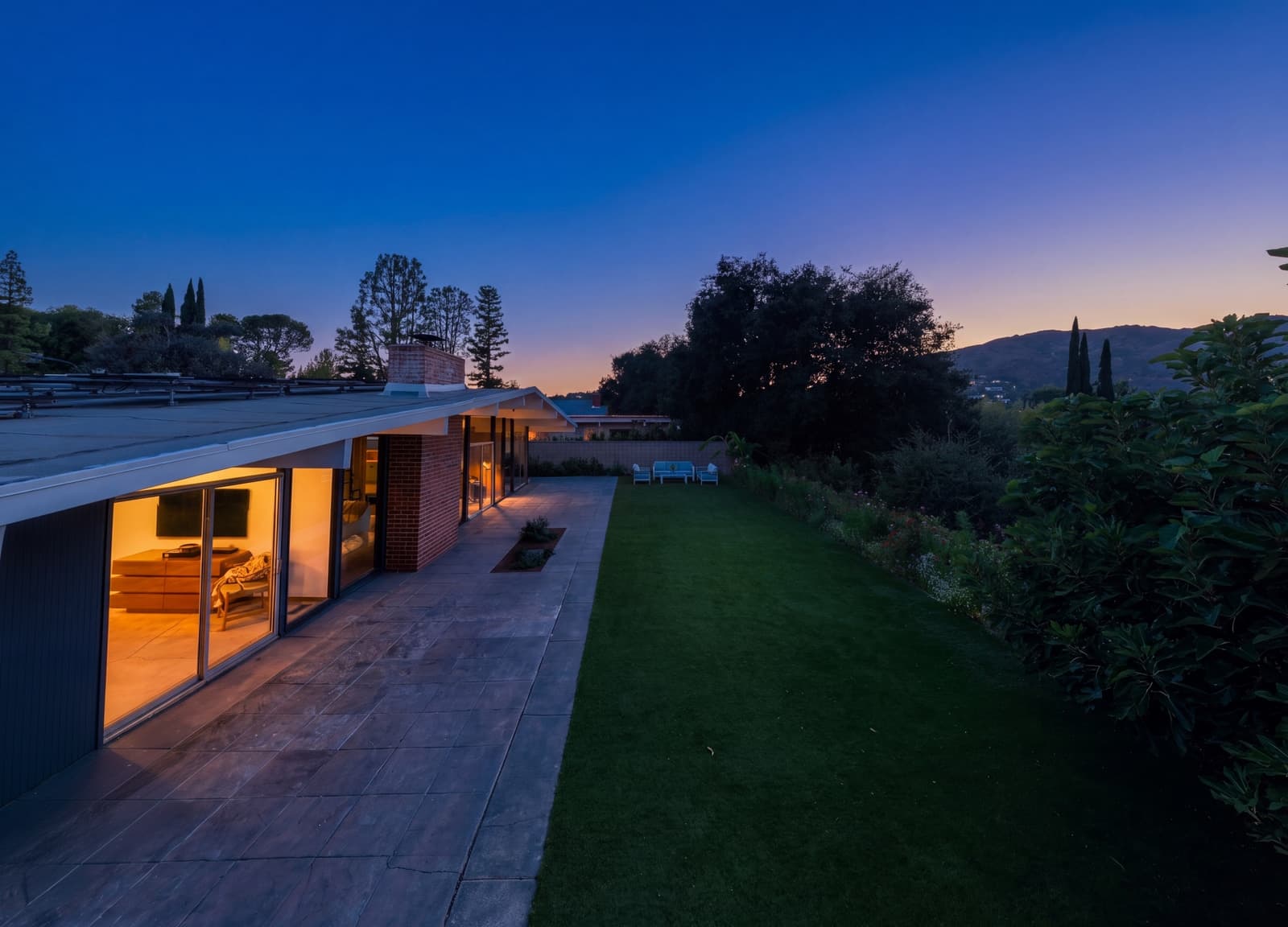 Lawn to a lit glass wall at twilight, deep blue sky above