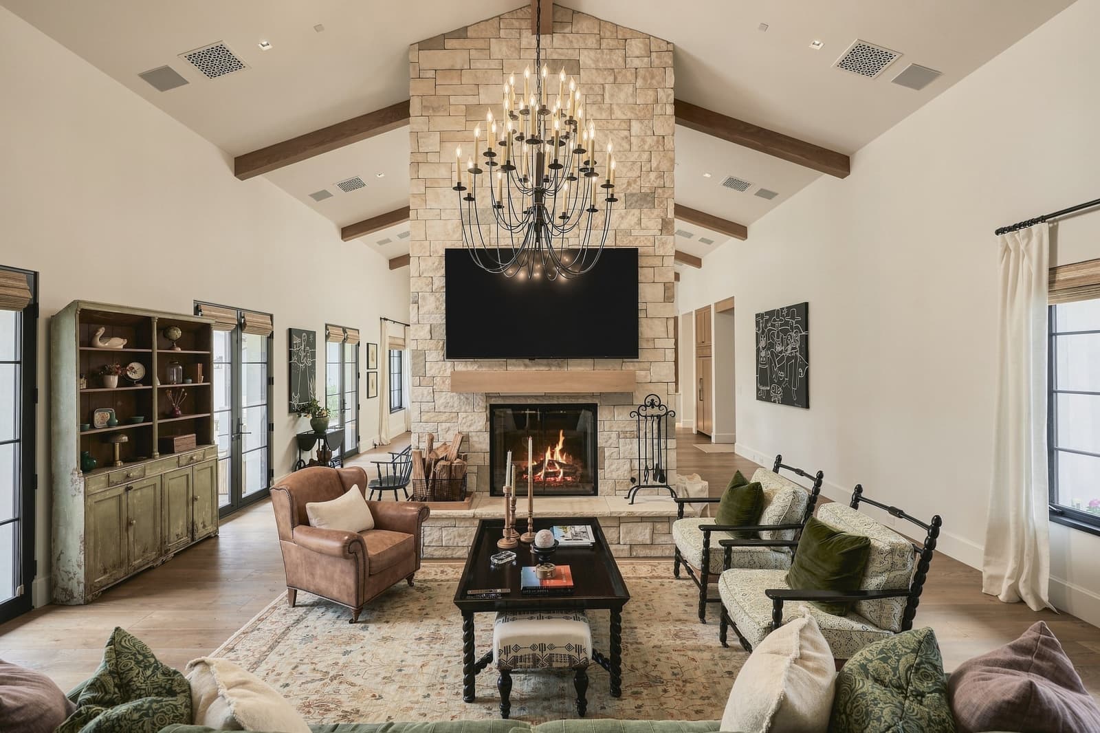 Great room with a stone fireplace, wood beams and a lit hearth