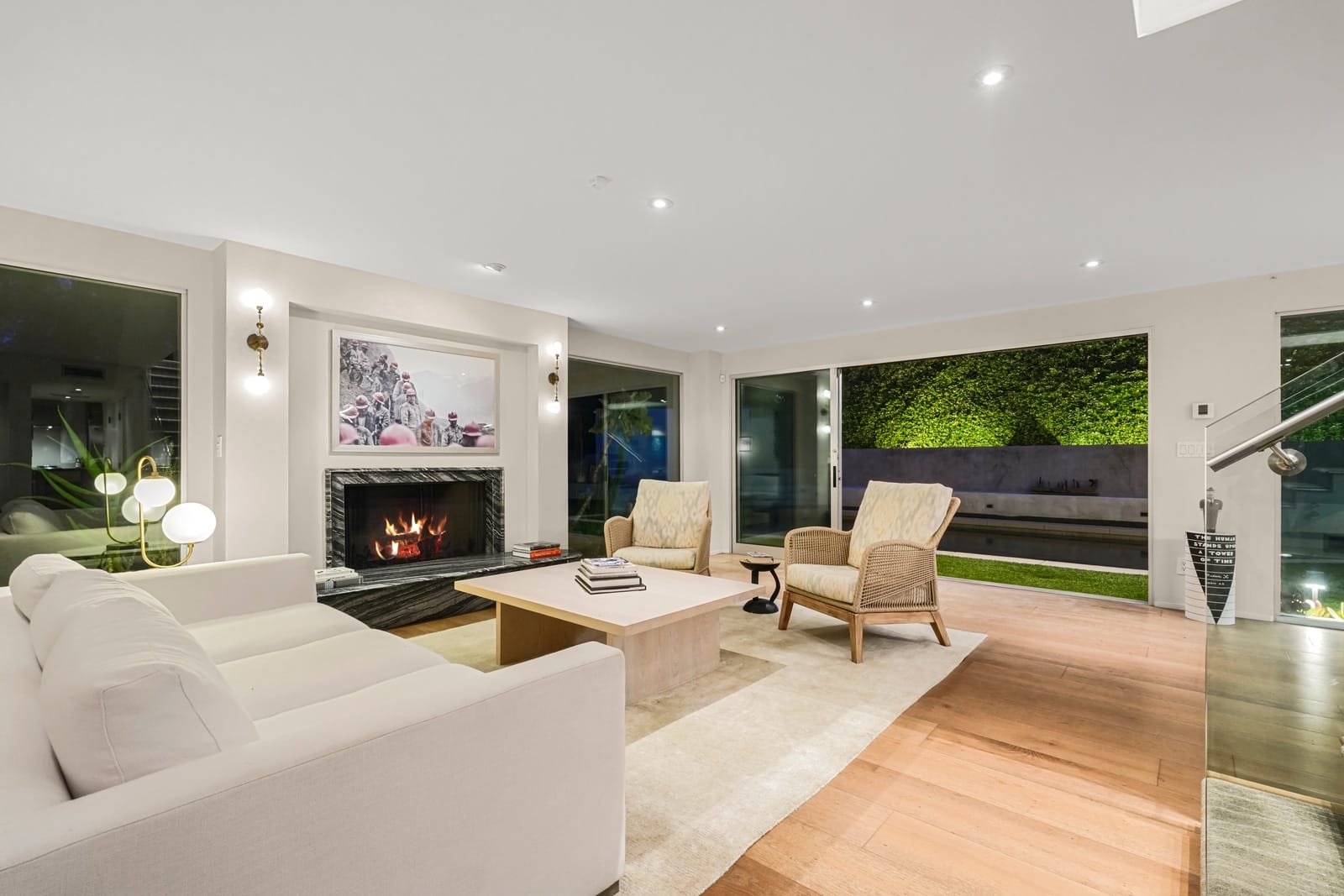 Living room at dusk, the fireplace lit and a planted wall glowing through the glass
