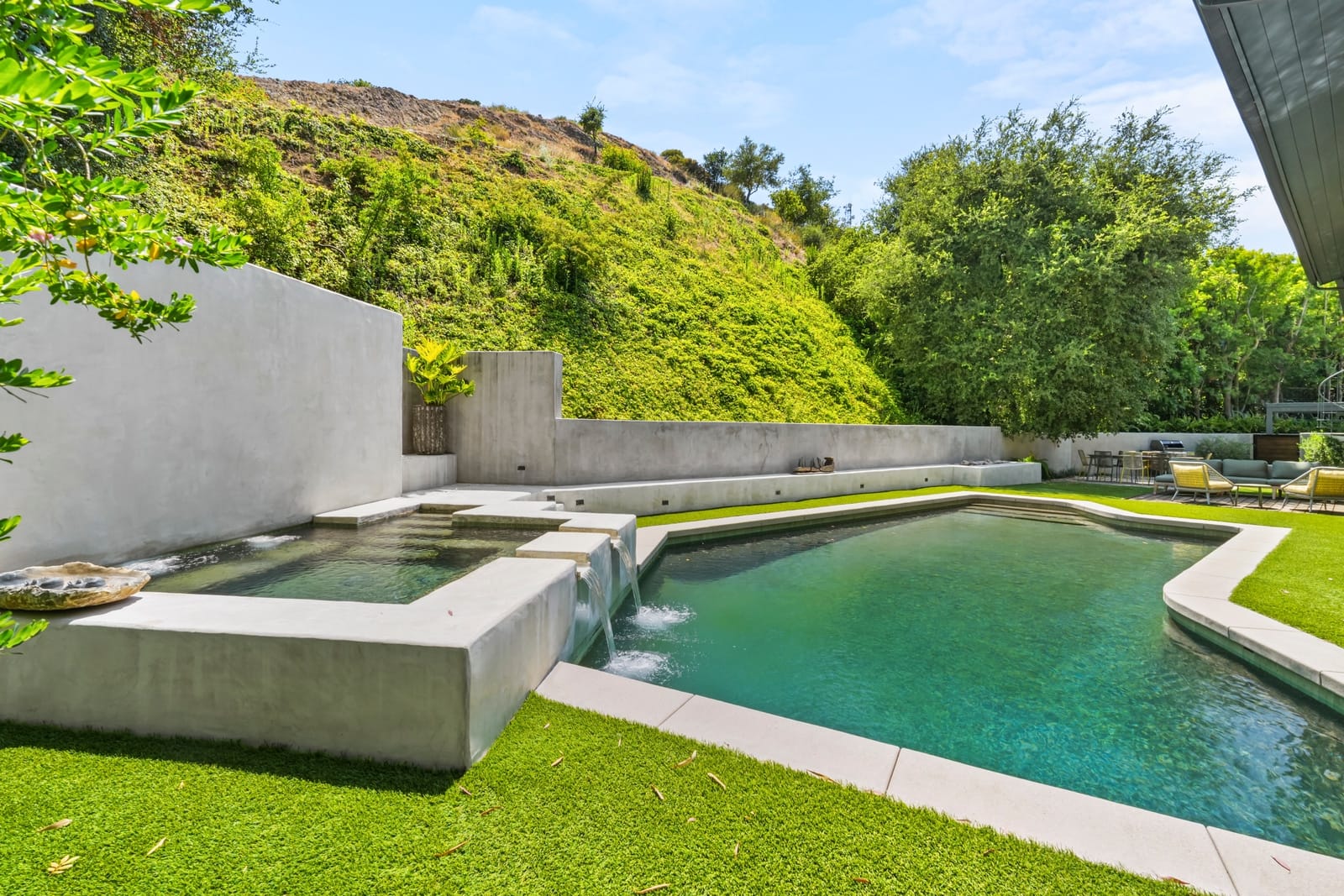 Pool with a concrete spillover spa against a green hillside