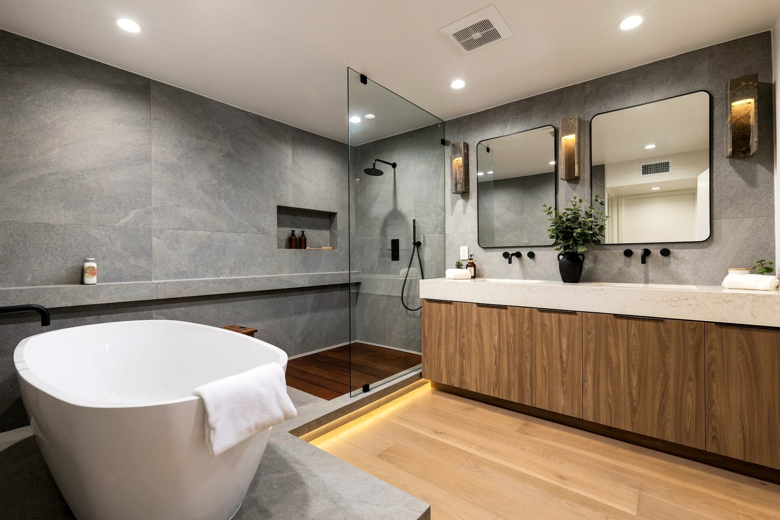 Grey stone bath with a freestanding tub and a lit walnut vanity