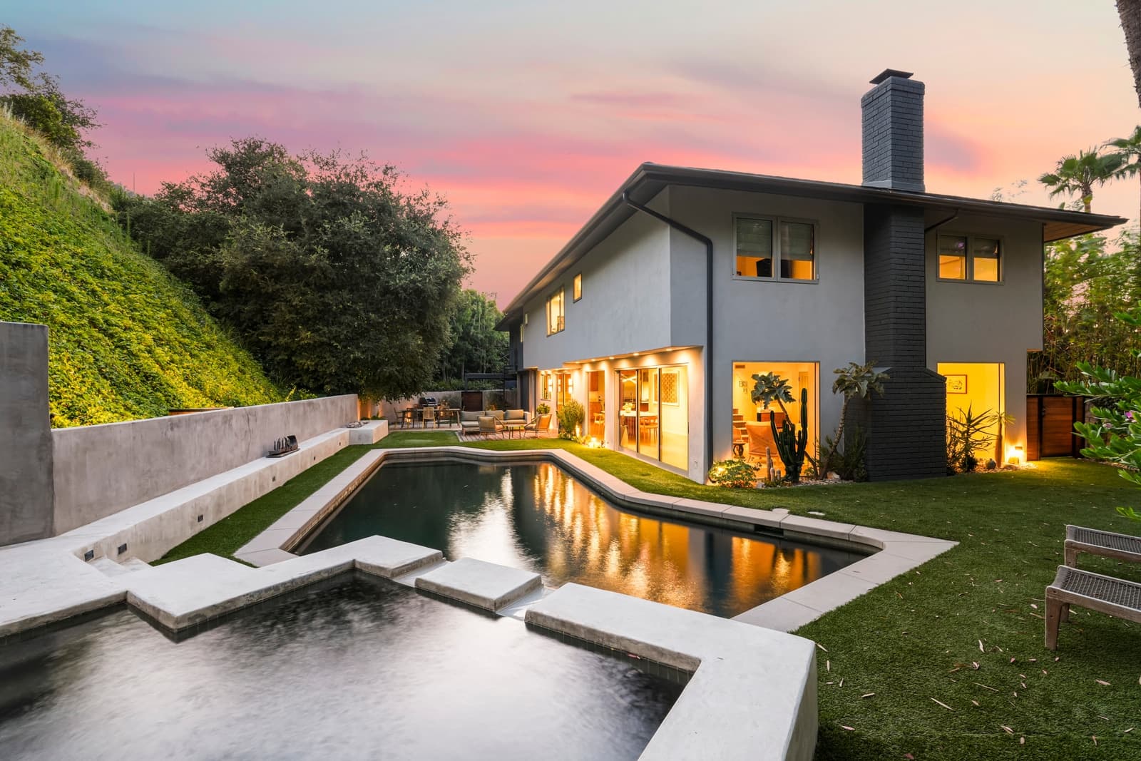 Hollywood Hills modern at twilight, every window lit, pool and hillside behind