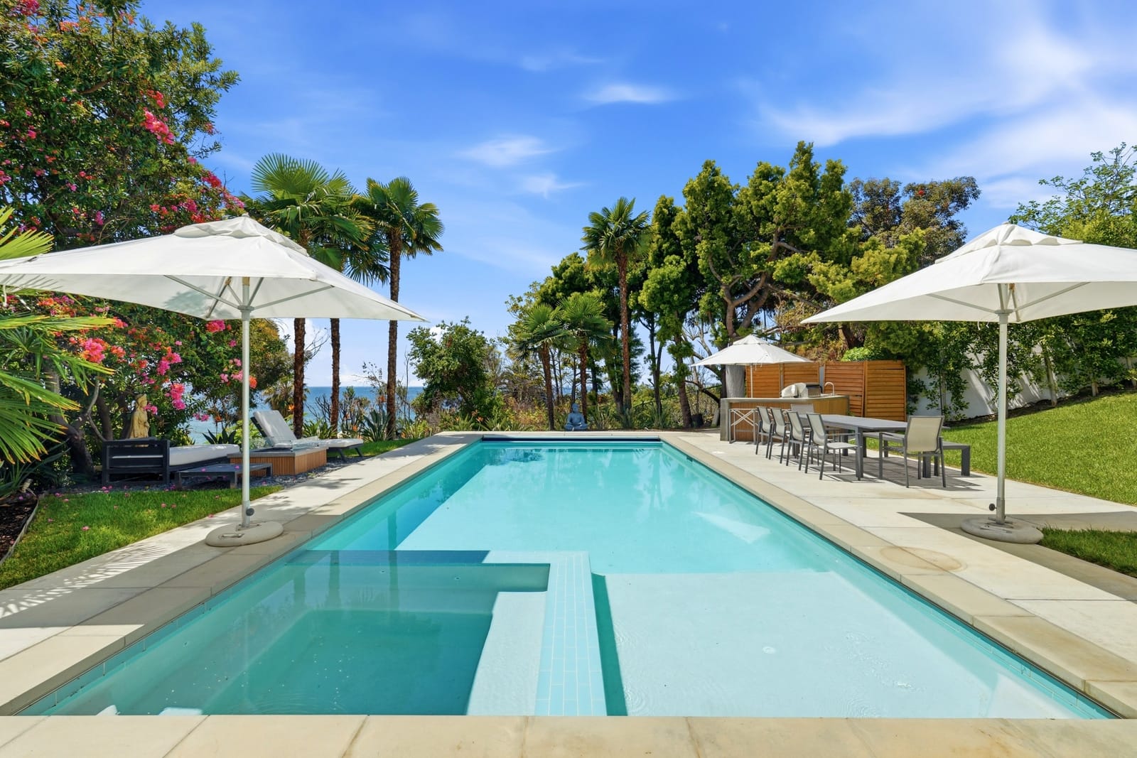Lap pool with white umbrellas and a lawn above the coast