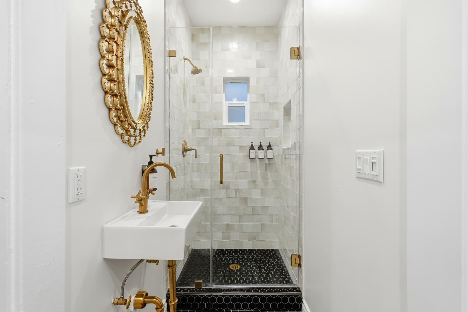 A marble shower with brass fittings and a sunburst mirror.