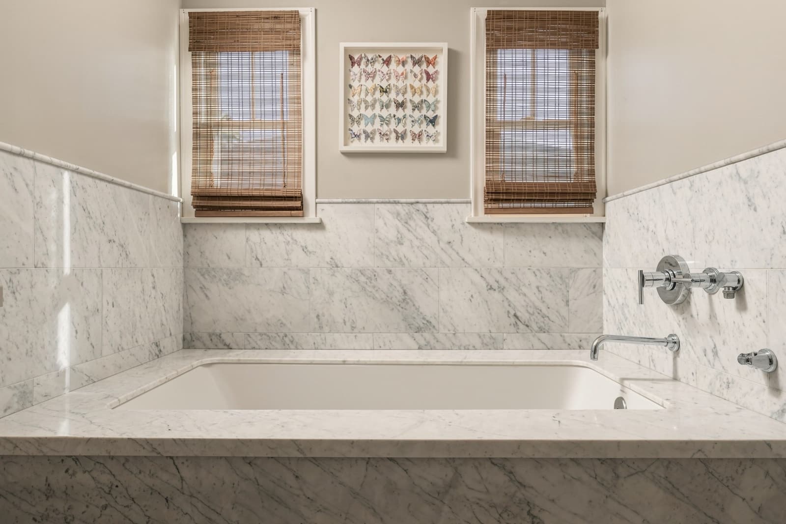 Marble soaking tub beneath woven window shades