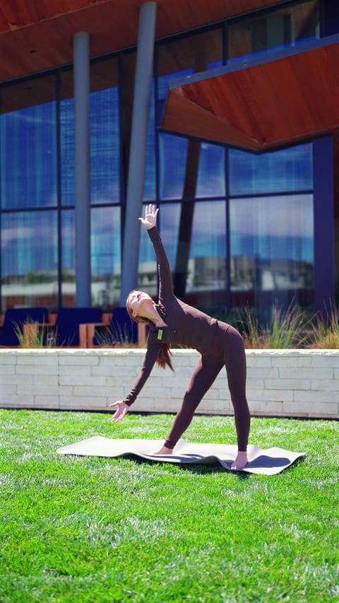 Amanda Grace doing yoga on a lawn in front of a glass building, from her brand reel