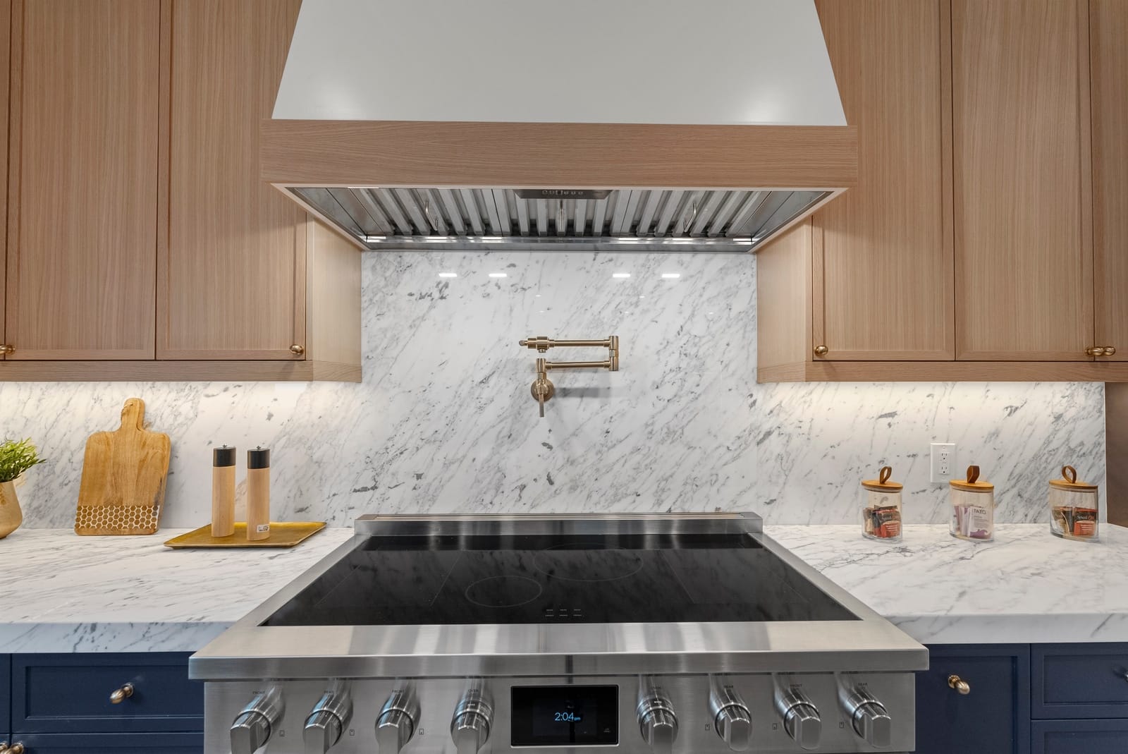 Range under a white hood with a marble backsplash and brass pot filler