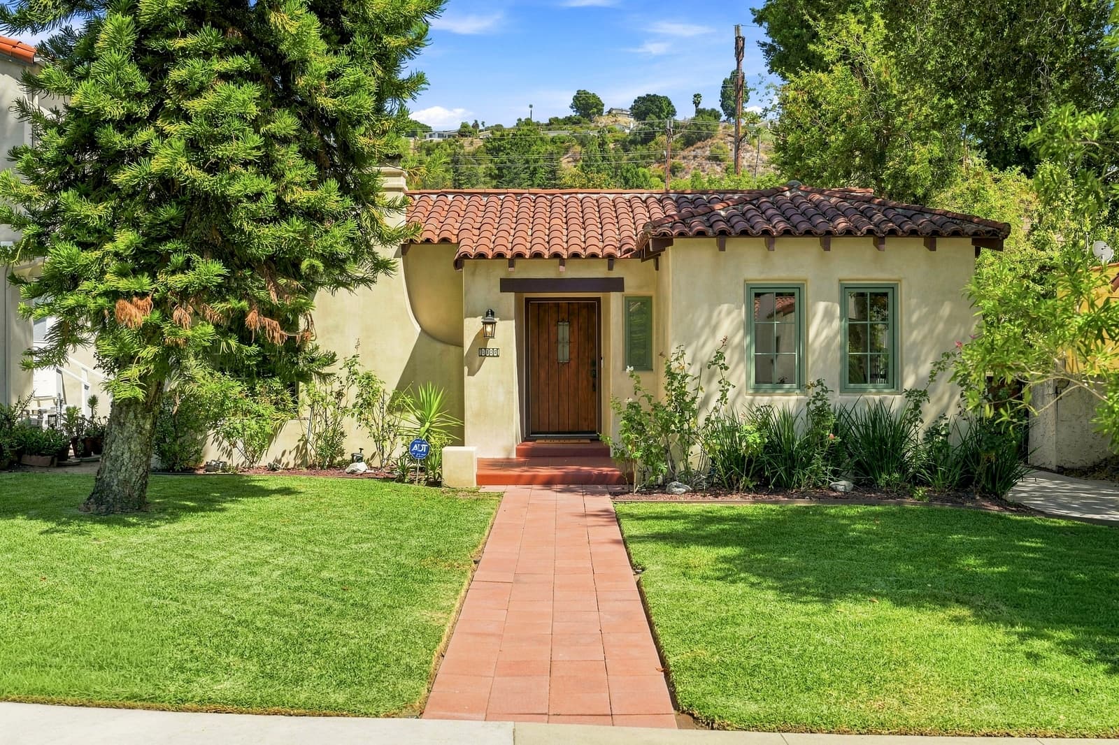 Spanish-style bungalow with a red tile roof and a tiled front walk, shot in daylight under a blue sky