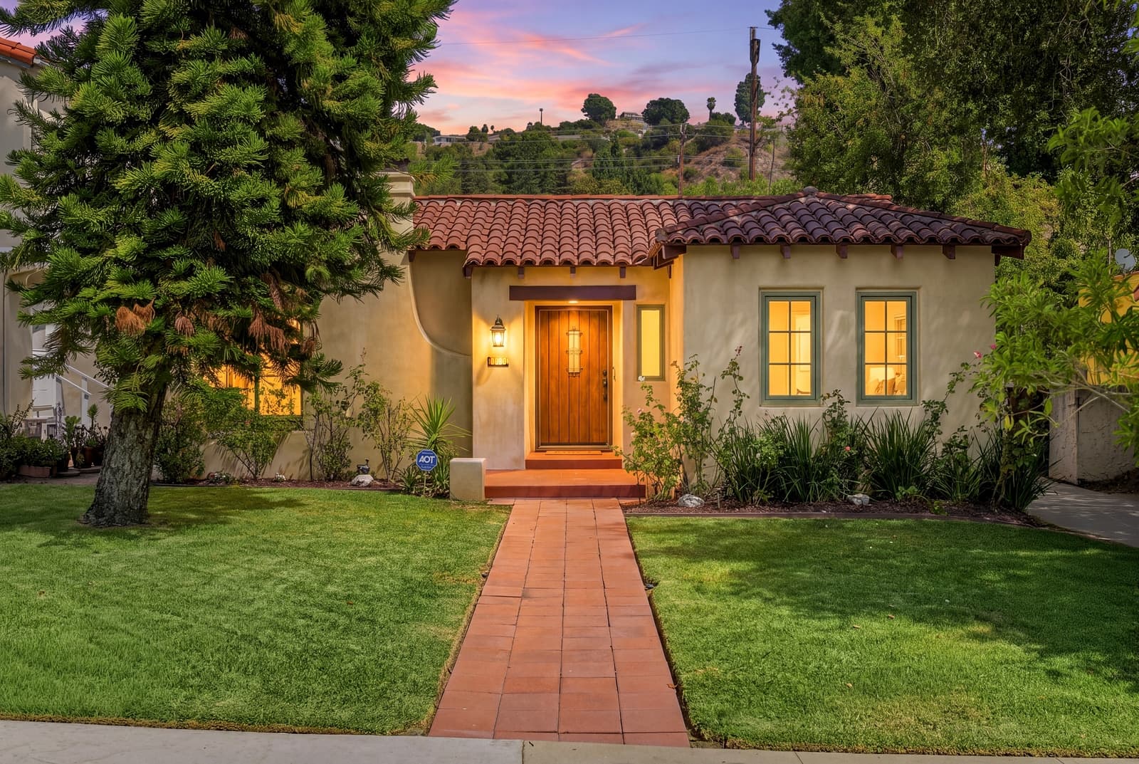 Spanish bungalow at virtual twilight, windows lit in the edit and labeled as virtual