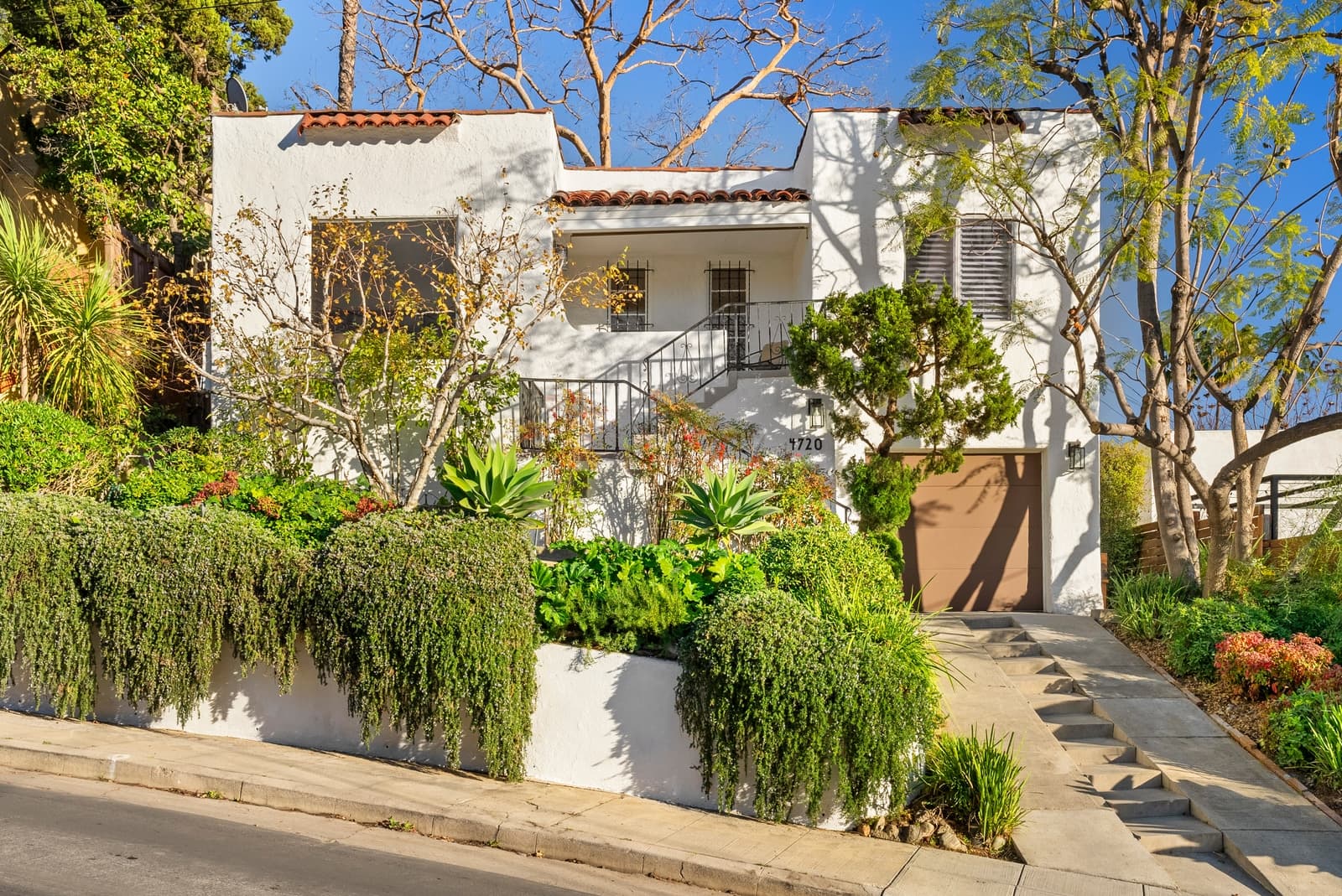 Spanish Revival home behind lush street-side landscaping
