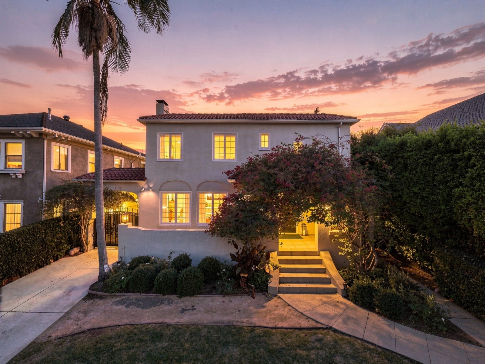 Spanish two-story at twilight, lit stairs rising through bougainvillea under a sunset sky
