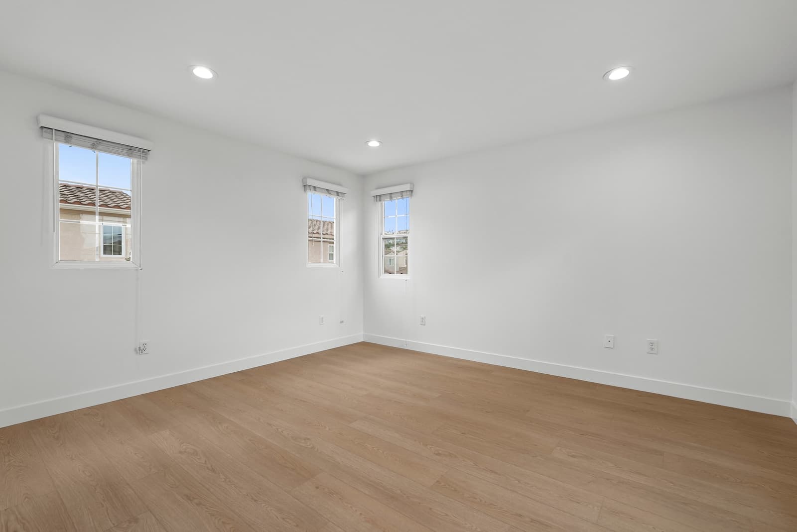 Empty bedroom with three windows and light oak floors