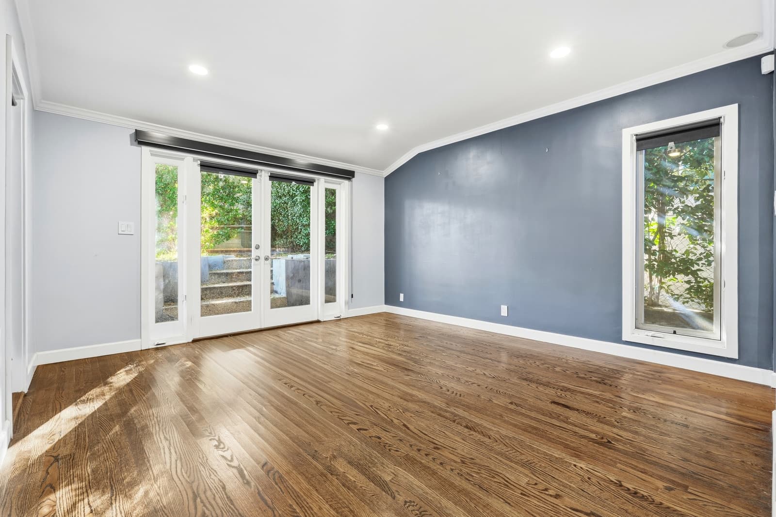 Empty bedroom with a slate-blue accent wall, French doors onto garden steps and wood floors