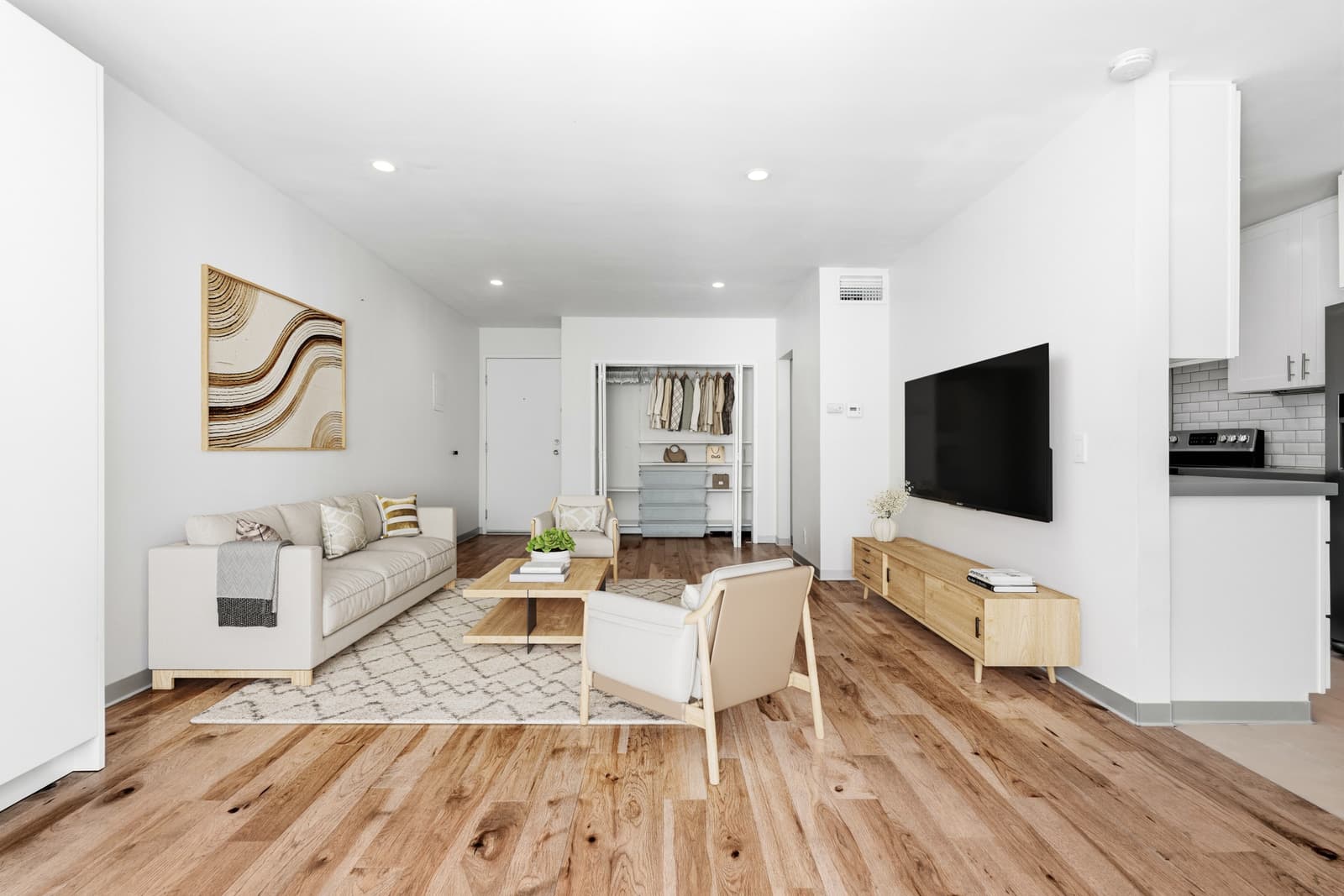 The same room virtually staged with a cream sofa, two wood-frame armchairs, a wood coffee table, a light wood media console under a wall-mounted TV and a patterned rug