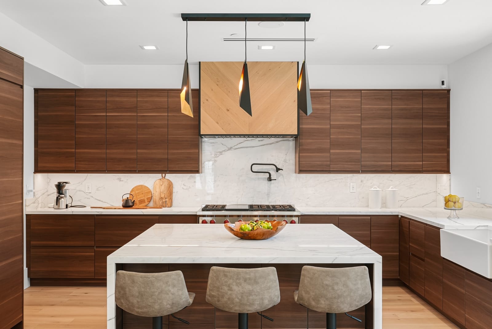 Walnut kitchen with a waterfall marble island and brass pendants, seen straight on