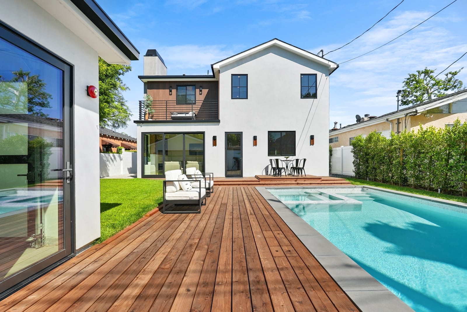 Pool and spa beside an ipe deck behind a white modern farmhouse