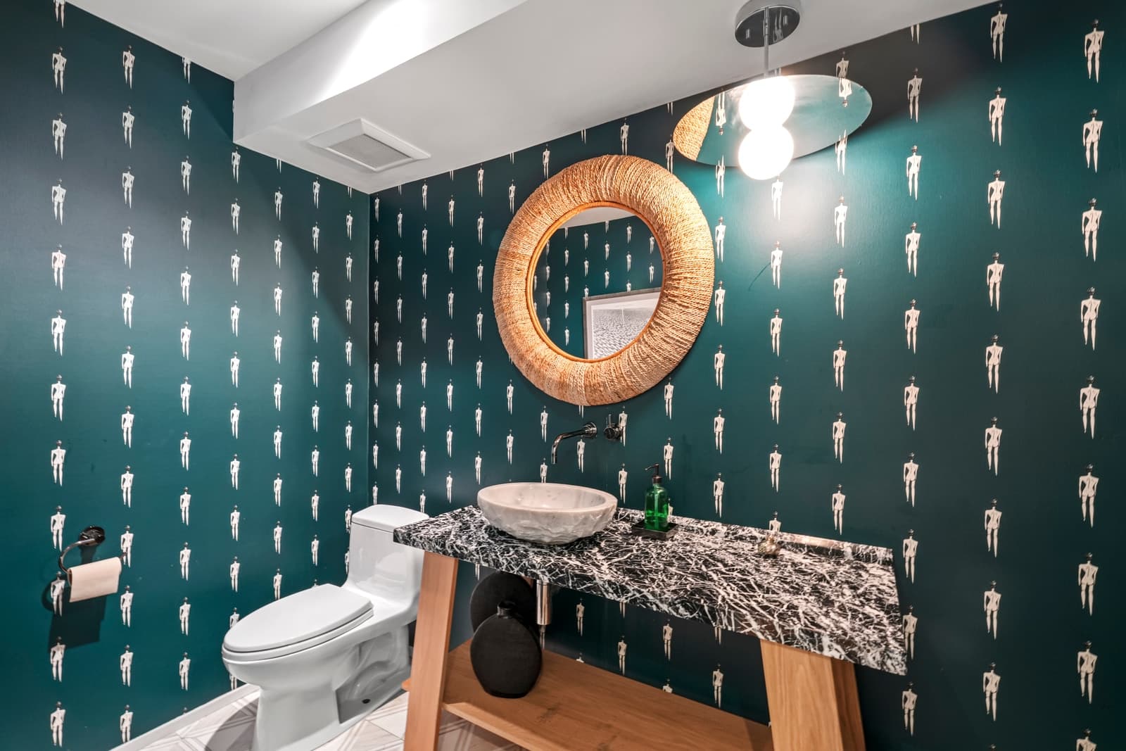 Powder room with teal patterned wallpaper and a round mirror