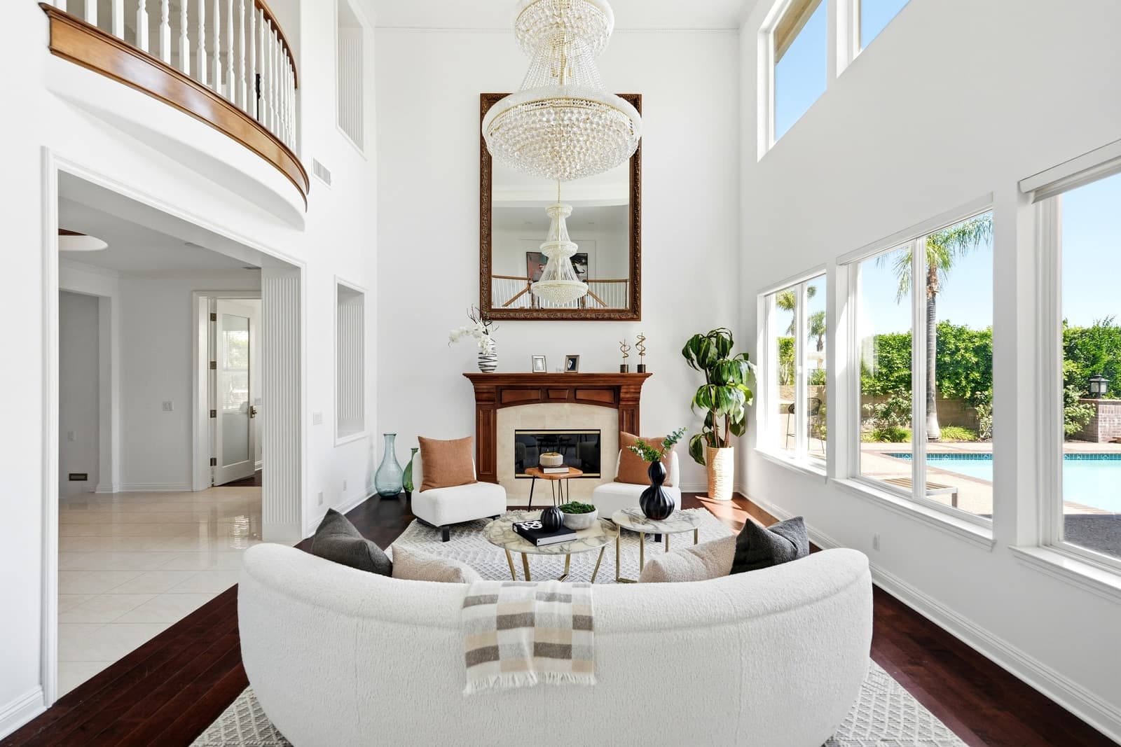 Two-story living room with a crystal chandelier, a curved white sofa and tall windows onto the pool