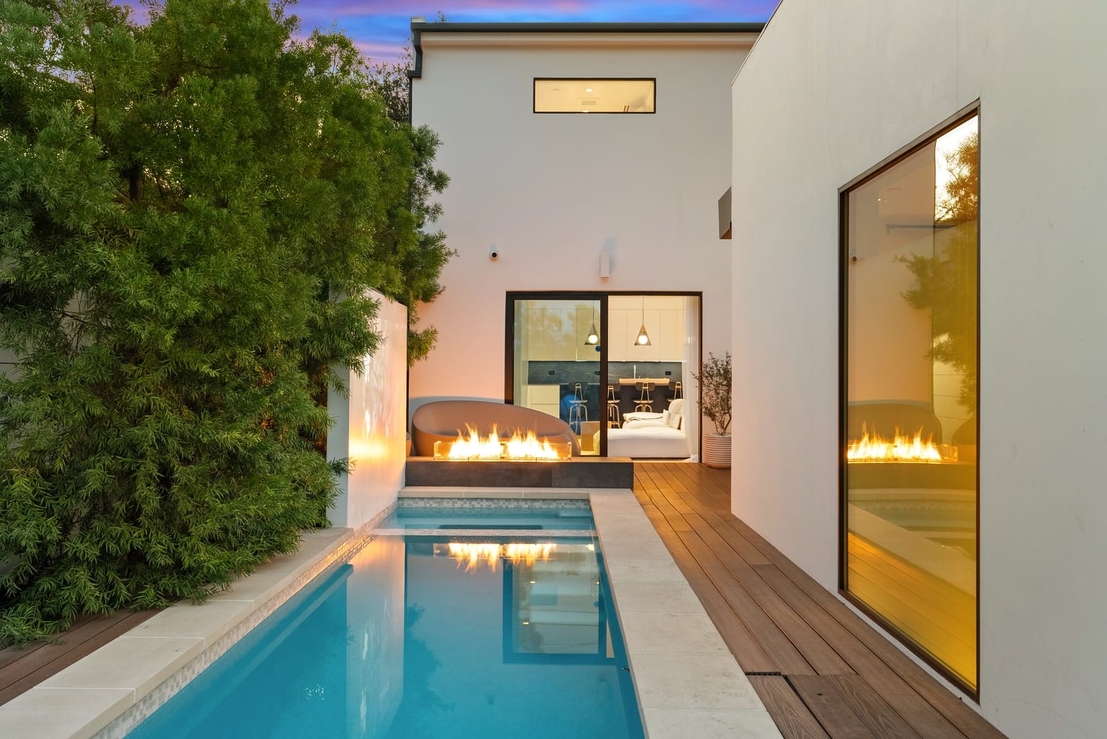 Lap pool at twilight with a fire line and a lit glass wall