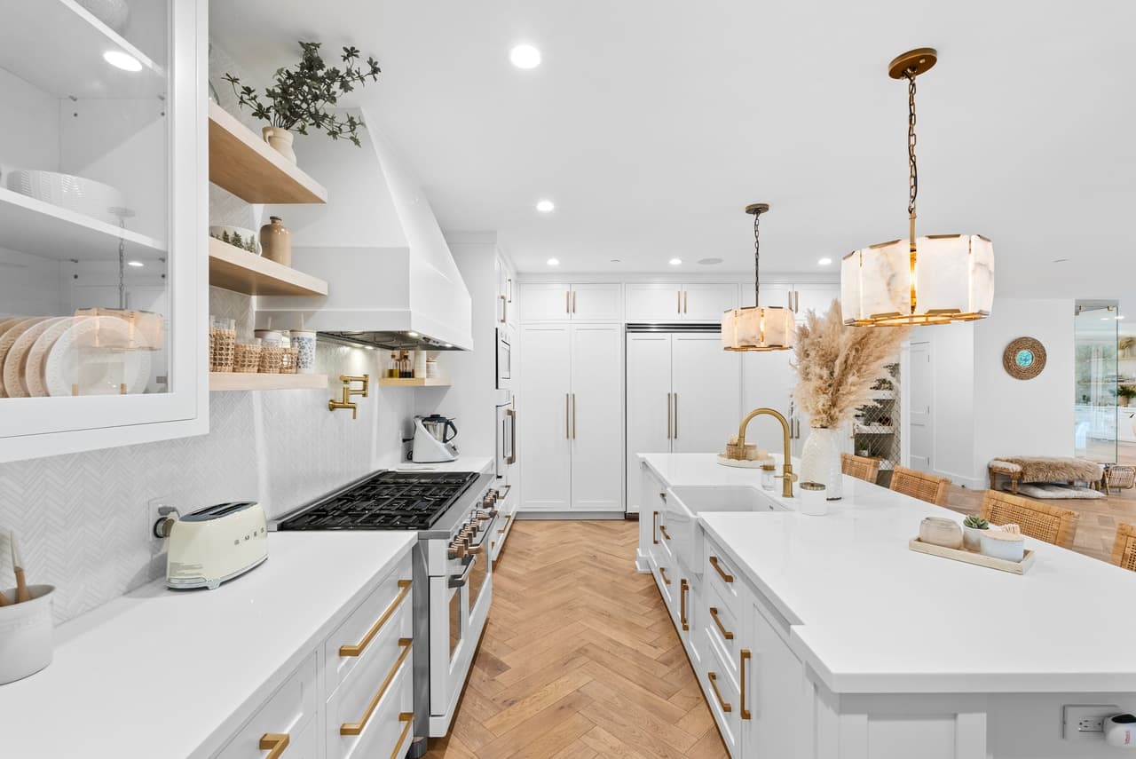 White kitchen with a herringbone wood floor, brass hardware and alabaster pendants