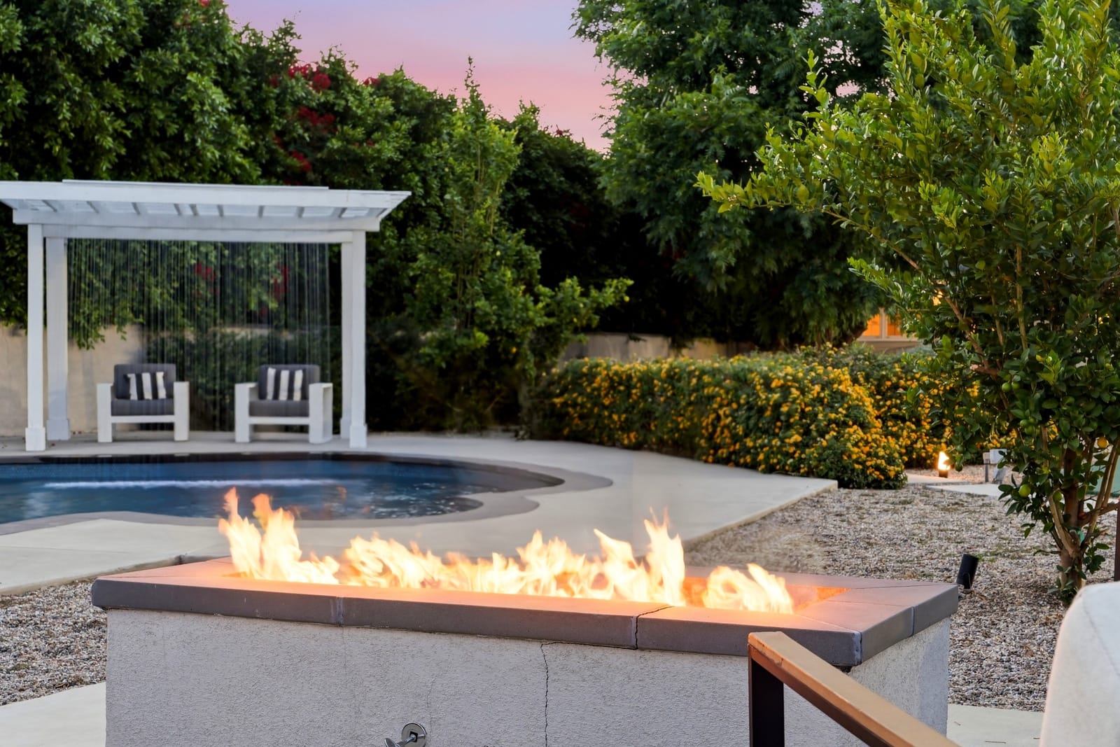 Fire table by the pool at dusk, white pergola behind