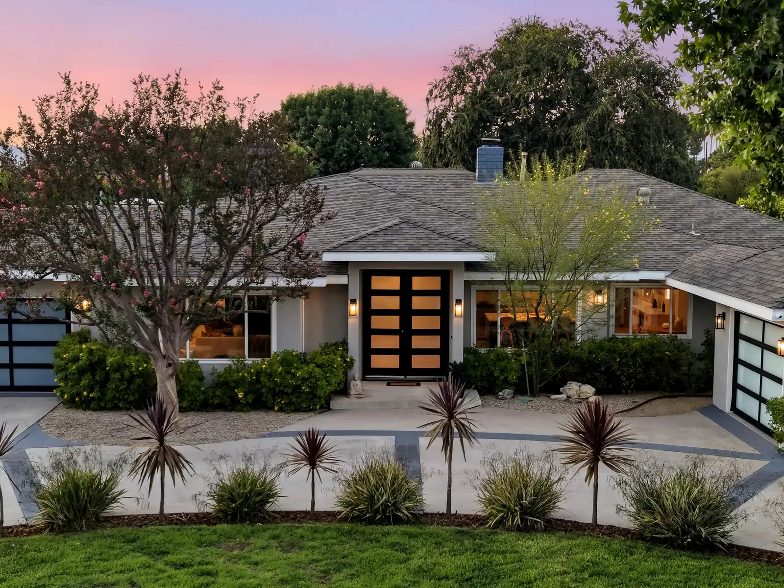Single-story ranch home at twilight with black double front doors and a front garden of spiky plants, Woodland Hills